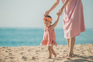 portrait of a mother is teaching her daughter walks on the beach