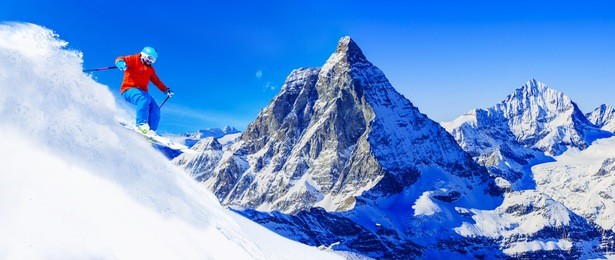 man skiing on fresh powder snow with matterhorn in background, zermatt in swiss alps.