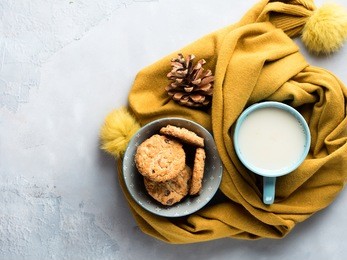 mug of tea with milk and cookies with chocolate chips in a soft yellow winter scarf on gray background. coffee break for home relax. top view