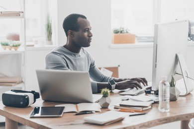 full concentration. handsome young african man working on the computer and smiling while sitting at his working place in creative office 