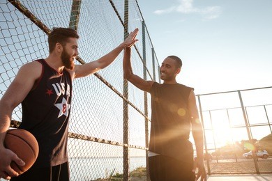 portrait of a two young sports men giving high five while playing basketball at the playground