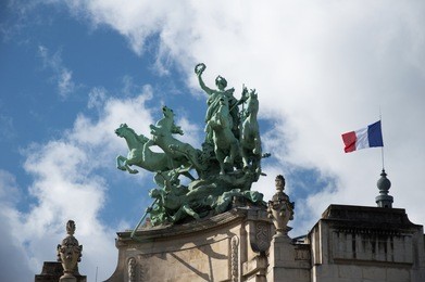 french flag and sculptures on top of the gran palace in paris
