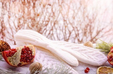 cozy winter scene with white knitted wool warm mittens, pomegranate, pine cones and orange slices. christmas morning decoration, copy space background, selective focus, toned