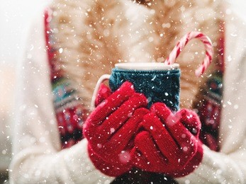 woman holding winter cup close up on light background. woman hands in red gloves holding a cozy mug with hot cocoa, tea or coffee and a candy cane. winter and christmas time concept