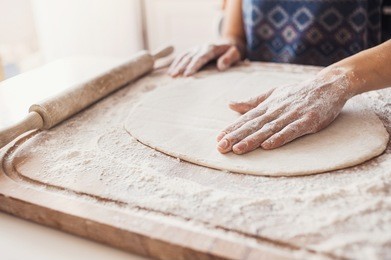 hands baking bread or pizza dough with rolling pin on wooden table