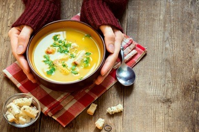 woman hands holding bowl of vegetable soup with parsley and croutons over wooden background - healthy winter vegetarian food