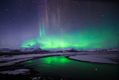 colorful northern lights (aurora borealis) and starry sky reflected over glacial lake and snow-covered mountains in iceland.