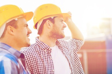 business, building, teamwork and people concept - group of smiling builders in hardhats with clipboard outdoors