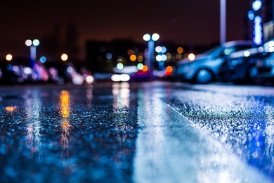 rainy night in the parking shopping mall, rows of parked cars. close up view from the level of the dividing line, image in the blue tones