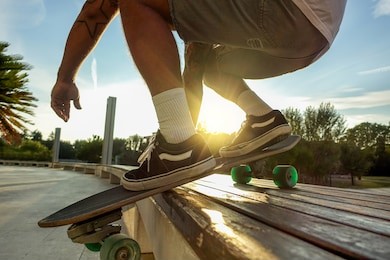 silhouette of young man performing with skateboard up wood bench at sunset in urban city park - skater having fun with back sunlight - extreme sport concept - focus on left shoe - warm filter