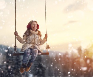 happy child girl on swing in sunset winter. little kid playing on a winter walk in nature.