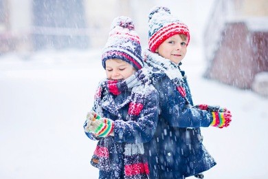 two little kid boys in colorful clothes playing outdoors during snowfall. active leisure with children in winter on cold days. happy siblings and twins having fun with snow