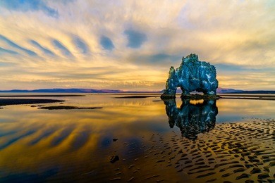 beautiful reflection with magical clouds on sandy beach at hvitserkur in iceland
