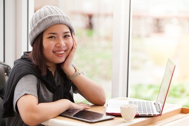 pretty female student with cute smile keyboarding something on net-book while relaxing after lectures in university, beautiful happy woman working on laptop computer during coffee break in cafe bar