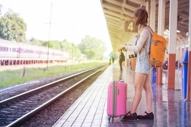 beautiful smiling woman traveler with luggage walking on the platform along the passenger train