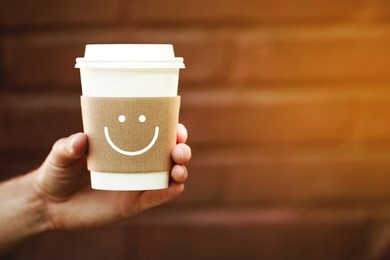 paper cup of happy takeaway coffee in the hand. holder with happy smile, because coffee is always a good idea. toning of evening sunlight.