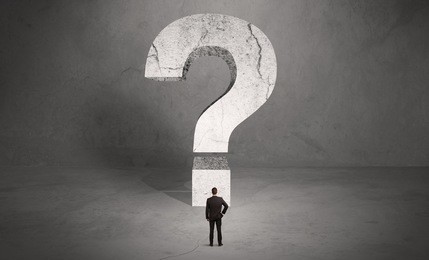 a small elegant business person in suit standing with his back in front of a huge question mark in open space concept