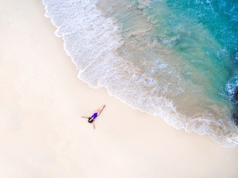 young woman in a violet bikini lying on the back on the sand near the waves of blue sea. top view. surin beach, andaman sea, phuket, thailand. aerial shooting.