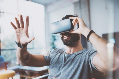 young bearded man wearing virtual reality glasses in modern interior design coworking studio. smartphone using with vr goggles headset. horizontal,flares effect, blurred background