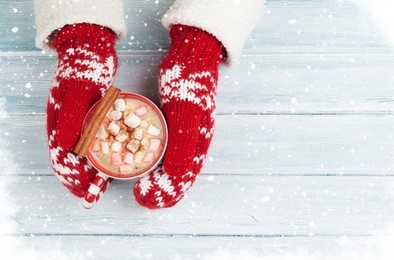 female hands holding hot chocolate with marshmallow above wooden table. top view with copy space