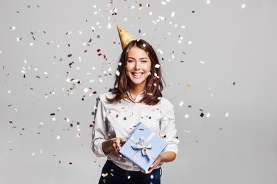 beautiful happy woman with gift box at celebration party with confetti falling everywhere on her. birthday or new year eve celebrating concept