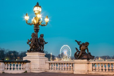lamp post on alexander iii bridge at dusk with ferris wheel on the background. it's a deck arch bridge, regarded as the most ornate, extravagant bridge in the city. 