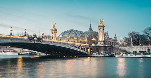 panoramic view of the the alexander iii bridge at dusk with grand palais (great palace) on the background. it's a deck arch bridge, regarded as the most ornate, extravagant bridge in the city. 