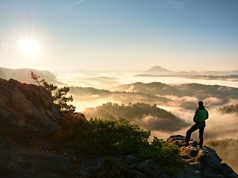 man silhouette stay on sharp rock peak. satisfy hiker enjoy view. tall man on rocky cliff watching down to landscape. vivid and strong vignetting effect.