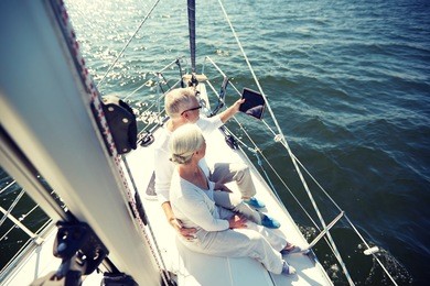 sailing, technology, tourism, travel and people concept - happy senior couple with tablet pc computer on sail boat or yacht deck floating in sea