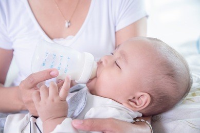 asian mother holding and feeding milk for her child from plastic bottle at home