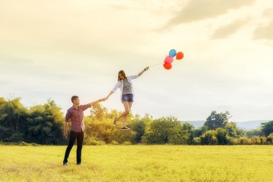 levitating woman with colorful balloon and with holding hand girlfriend. image vintage at sunset