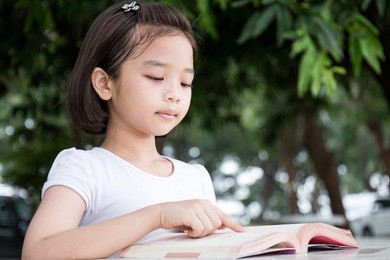 little asian child reading a book outdoor