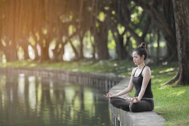 young woman doing yoga in morning time with the sun lighting in the park with pond