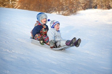 two joyful childred sledding down the hills on a winter day.