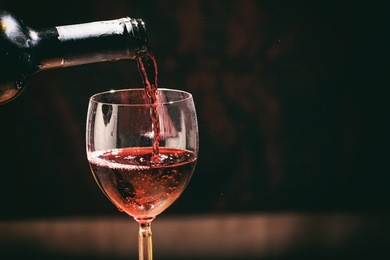 red wine bottle pouring wine in a glass on a dark background