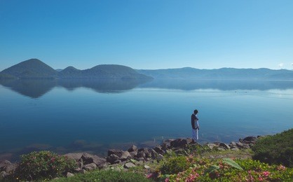 a japanese man to standing alone on the rock seeing natural view toya lake with blue sky, hokkaido, japan