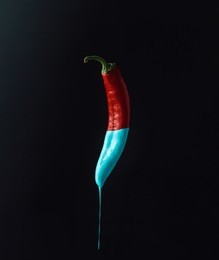 red pepper with dripping blue paint on dark background. minimal food concept.