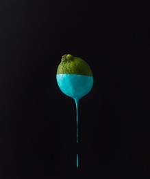 lime with dripping blue paint on dark background. minimal food concept.