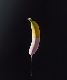 banana with dripping pink paint on dark background. minimal food concept.