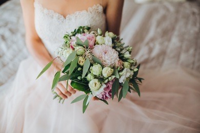 bride in dress sitting on bed and holding wedding bouquet of flowers and greenery
