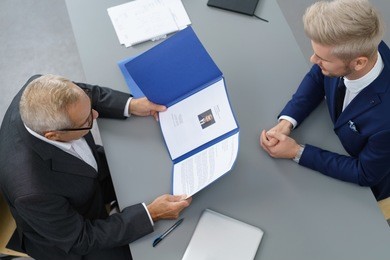 employer interviewing a young male job seeker for a business vacancy sitting at a table reading his cv viewed from above