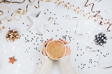 female hands holding cup of coffee on white rustic sparkling background. festive backdrop for holidays. flat lay style.