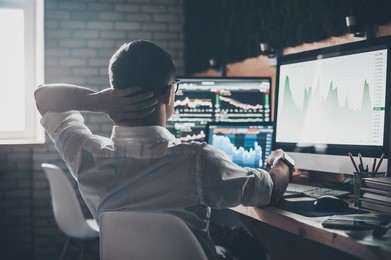 thinking about new solutions. rear view of young man in casual wear holding hand on the back of the head and working while sitting at the desk in creative office
