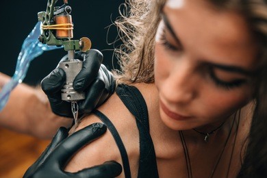 tattooing. pretty girl getting a shoulder tattoo. focus on tattoo machine. toned image