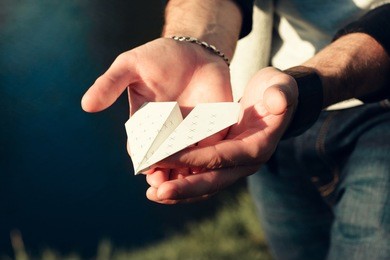 paper airplane in male hands close-up. man holding origami plane in palms outdoor near river. hobby, leisure, entertainment, handmade, craft concept