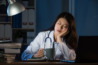 exhausted medical personnel sleeping with coffee after night shift at late night. pretty mixed race asian chinese woman model. medical and health concept