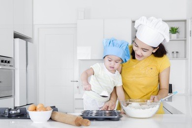 portrait of cute child learns holding a spoon with flour while making cookie in the kitchen 