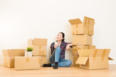 beautiful smiling woman moving house, holding the phone with open cardboard box. mixed race asian chinese model.