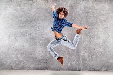 young urban hip hop dancer jumping and dancing with grunge concrete wall background. girl with afro hair.
