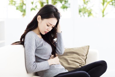 young woman sitting on sofa and having stomachache
